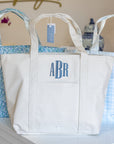 White tote bag with 'ABR' monogram on a shelf with other bags in the background.