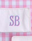 Two white textured pouches with 'SB' monogram on a pink checkered background