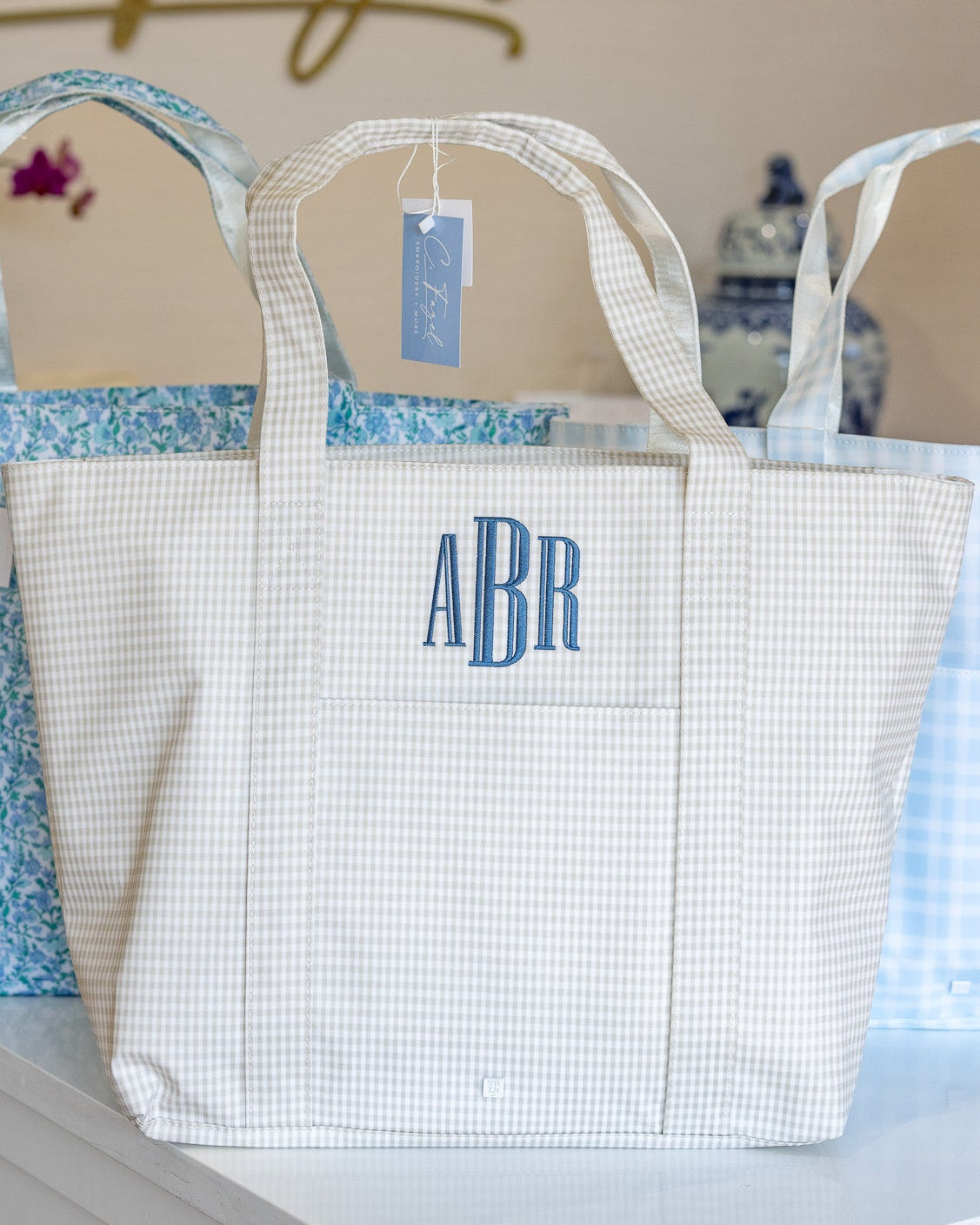 White tote bag with 'ABR' monogram on a shelf with other bags in the background.