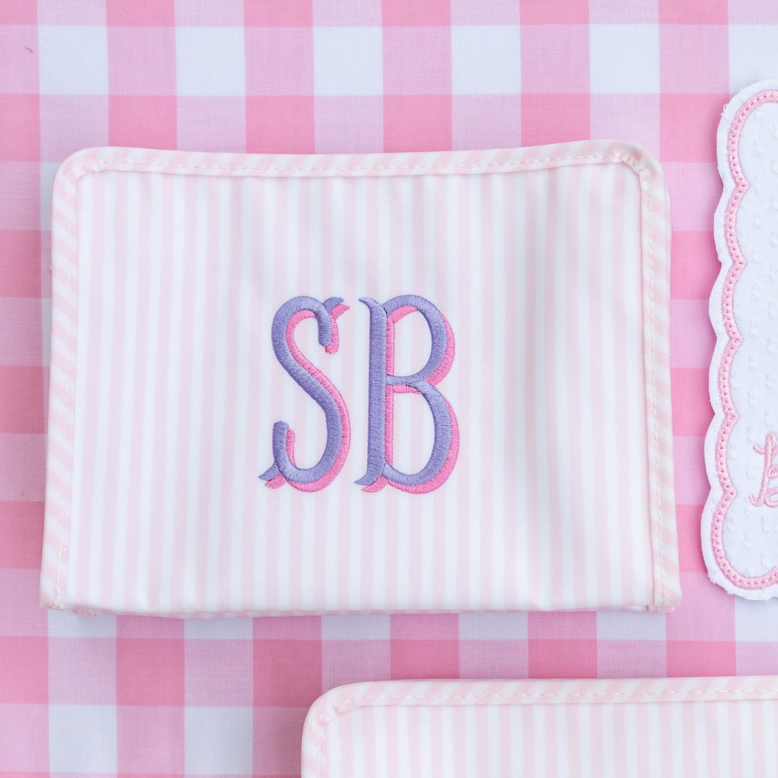 Two white textured pouches with 'SB' monogram on a pink checkered background