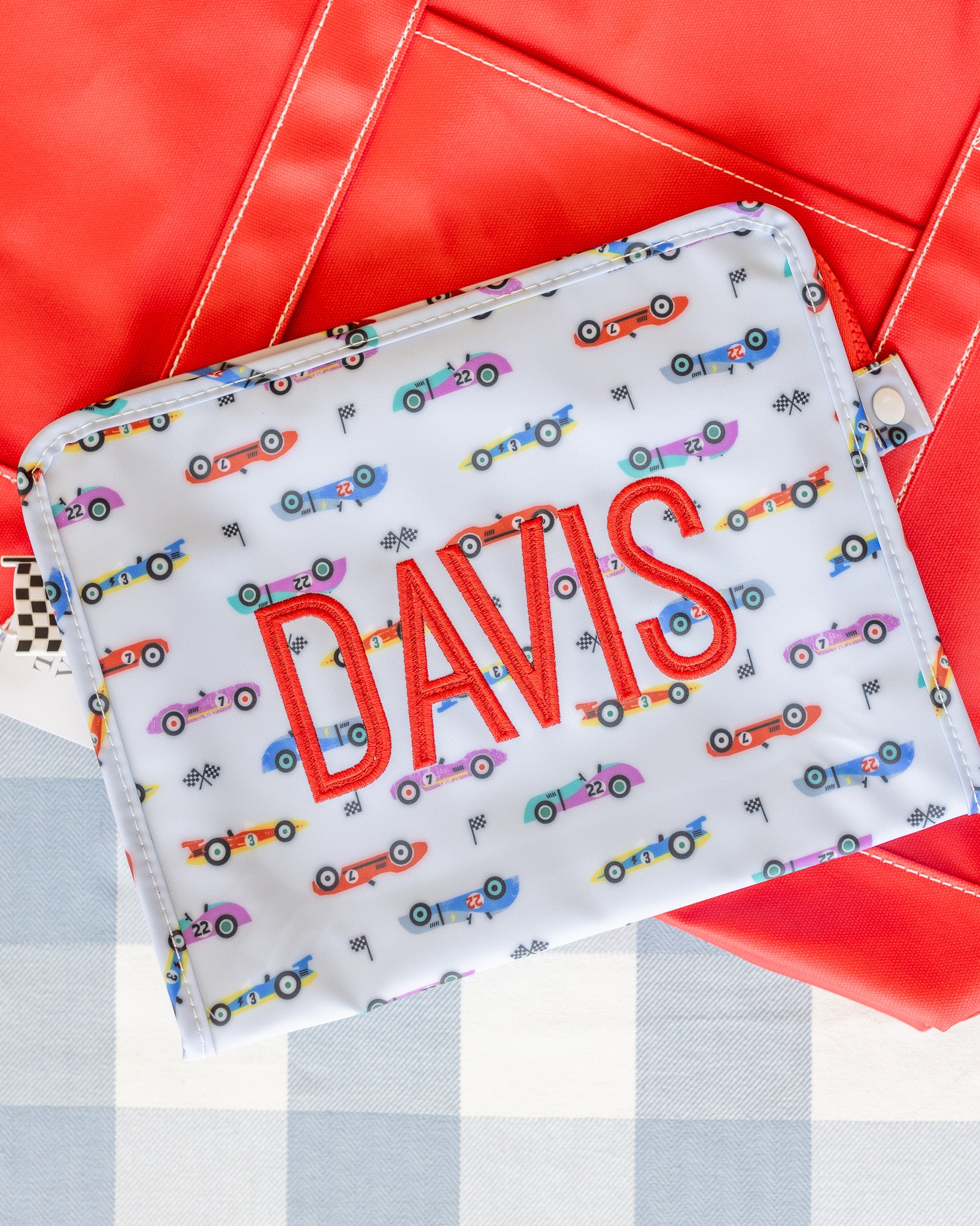 Fabric pouch with 'DAVIS' printed on it and car pattern, against a red and gray background.