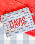 Fabric pouch with 'DAVIS' printed on it and car pattern, against a red and gray background.